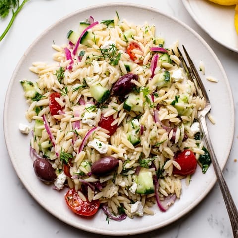 Freshly prepared Greek Orzo Salad featuring tender orzo pasta, crisp vegetables, and briny feta cheese, ready for a sunny picnic or potluck.