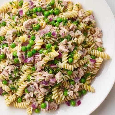 A close-up view of Lemony Tuna Pasta Salad, featuring flaked tuna, red onion, and bright peas tossed in olive oil.