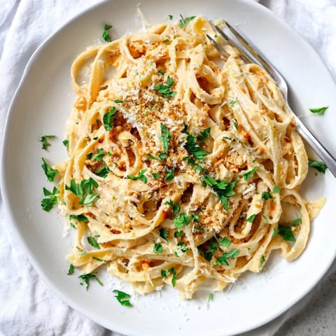 A steaming skillet of Sriracha Honey Pasta, tossed in a glossy sweet-spicy sauce, garnished with fresh parsley and parmesan.