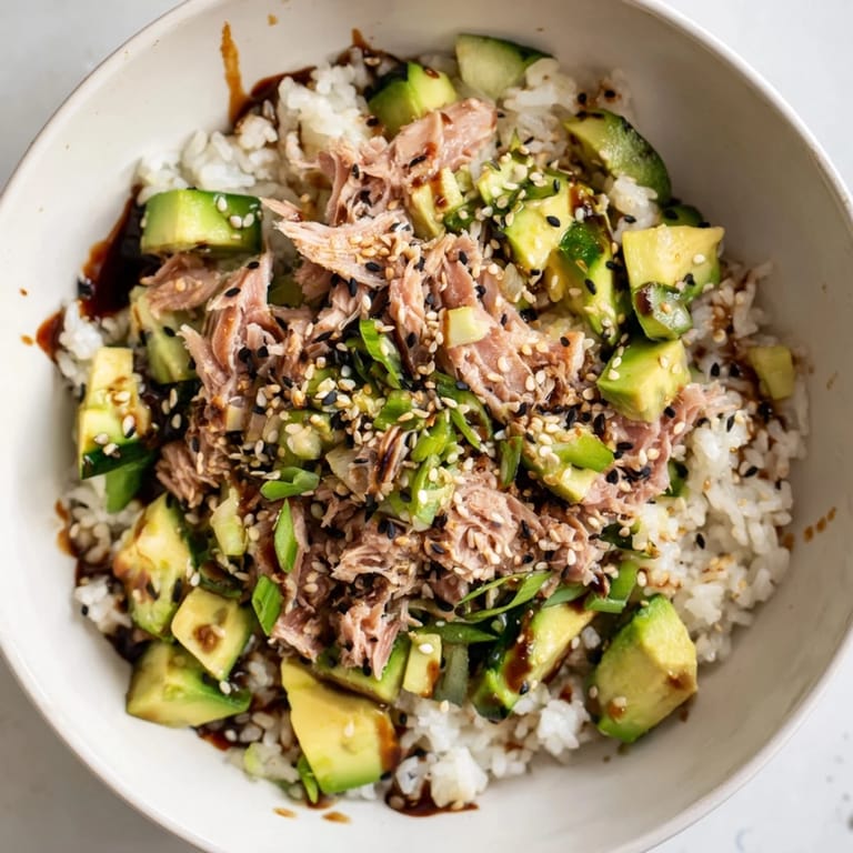 Colorful Tuna Avocado Rice Bowl featuring Japanese-inspired flavors, with nori strips, sriracha drizzle, and fresh cilantro on warm, fluffy rice for an easy weeknight meal.