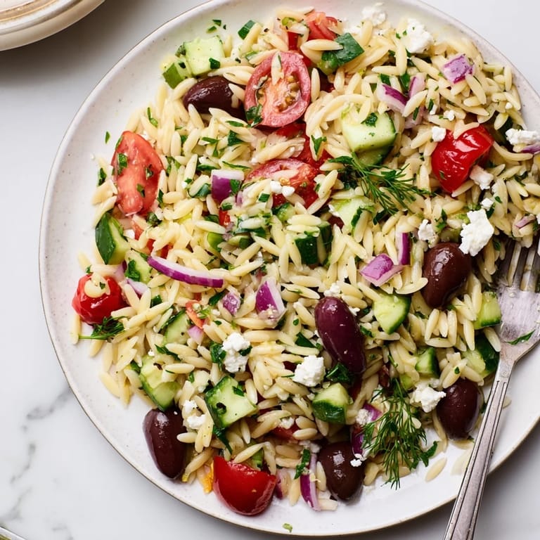 Colorful Greek Orzo Salad served in a white bowl, highlighting juicy tomatoes, diced cucumber, red onion, and olives in a bright vinaigrette.